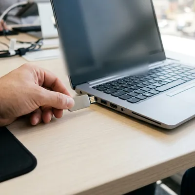 Chave de segurança corporativa sendo encaixada na porta USB de um notebook, sobre mesa de escritório