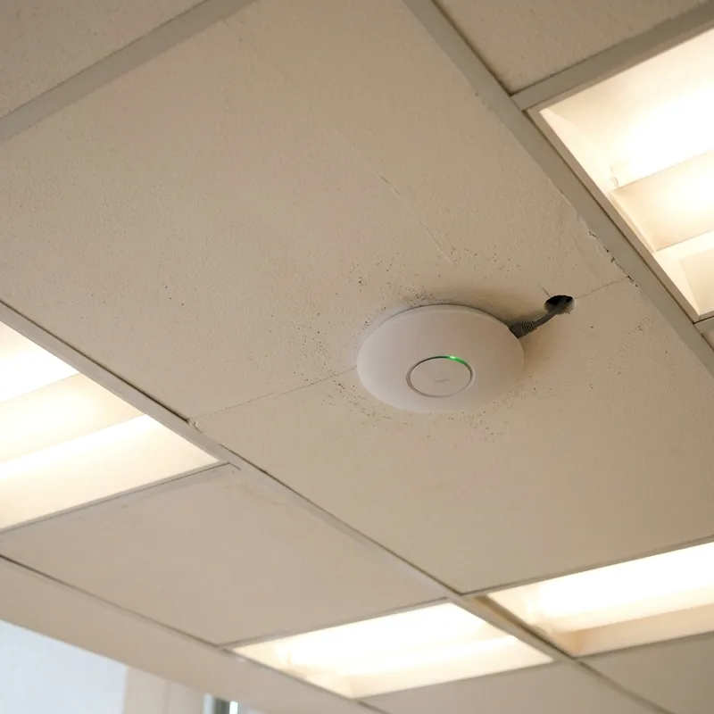 Ponto de acesso Wi-Fi empresarial instalado no teto de um ambiente corporativo