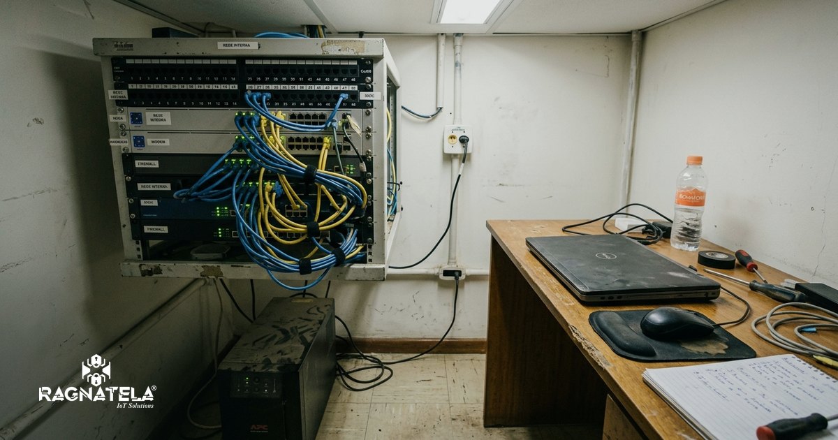 Rack de rede aberto em sala técnica de empresa, com switch, firewall, cabos azuis e amarelos organizados e luzes verdes de status acesas.